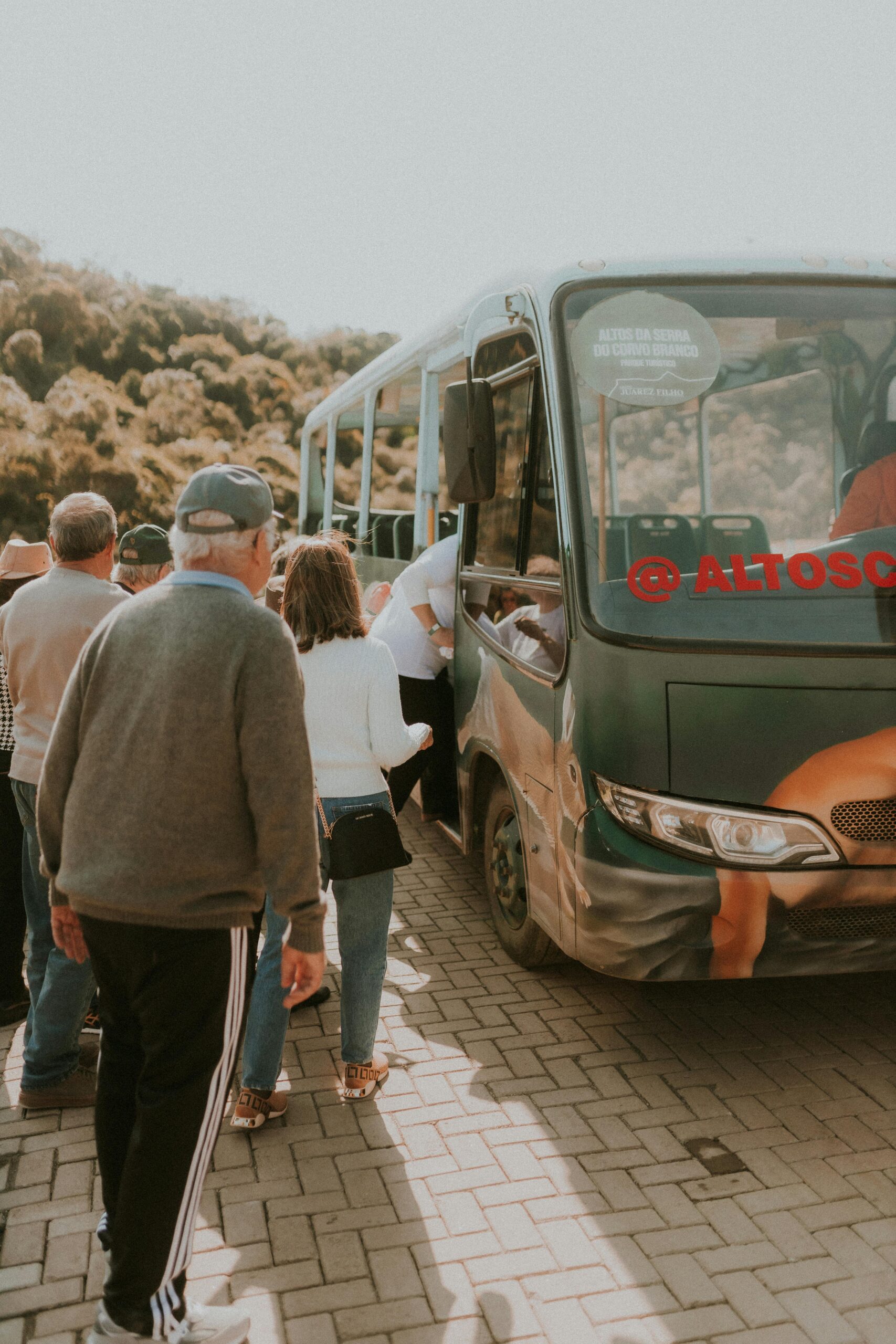 Group of people boarding a bus surrounded by nature, showcasing travel and transportation.